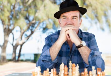 A man in a hat and checkered shirt looks contemplative as he plays a game of chess