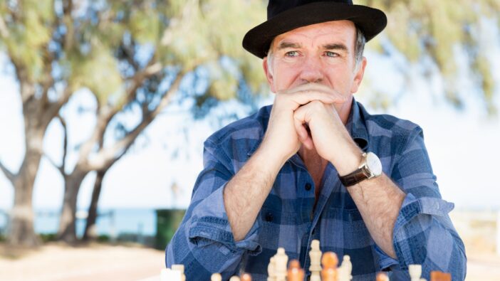 A man in a hat and checkered shirt looks contemplative as he plays a game of chess