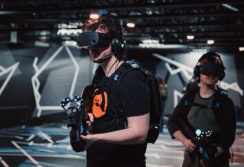Two men in a dark room playing a VR game wearing gaming clothing