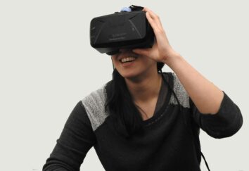 A woman in a black hoodie and VR glasses laughs during a game