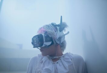 A woman wearing a white gown is in a foggy room wearing VR glasses